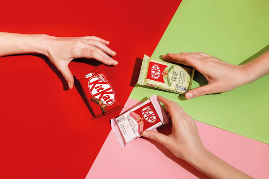 Hands exchanging Japanese KitKats with unique flavors on colorful background, showcasing Japan's innovative dessert culture.