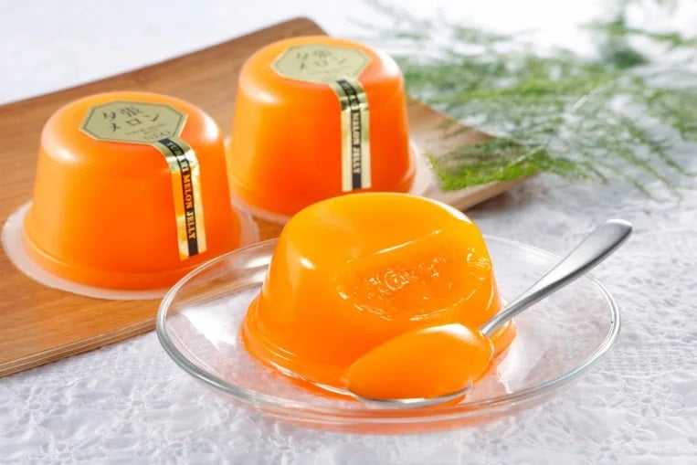 Yubari Melon Jelly NEO in vibrant orange, served with a spoon, showcasing its pulpy texture and rich flavor on a glass plate.