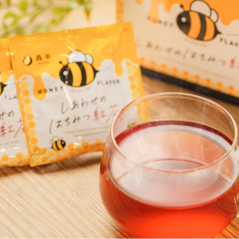 Glass of Morihan Black Tea Honey Flavor with tea bags in background showcasing honey bee design packaging.