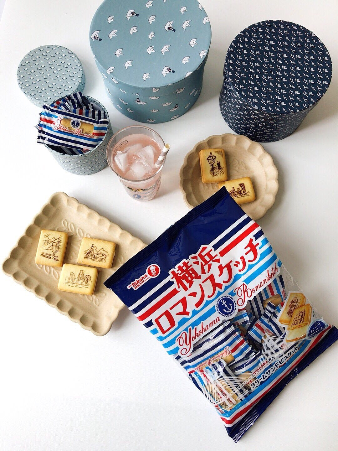 Yokohama Romance Cookie package with biscuit featuring Yokohama landmarks, accompanied by decorative boxes and a glass of iced drink.