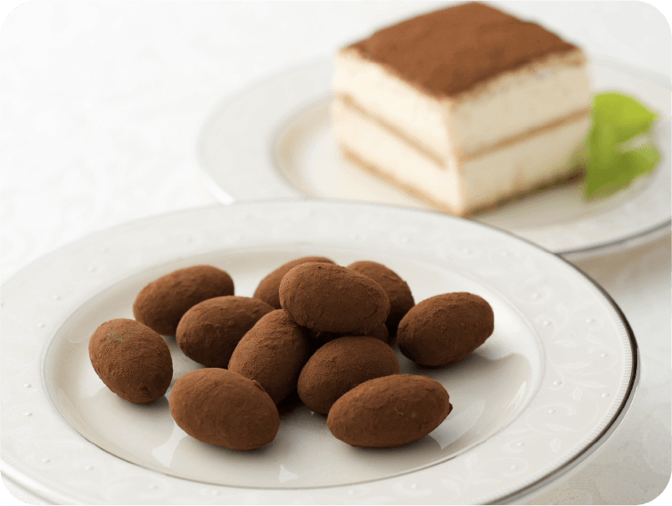 Plate of tiramisu chocolates with almonds and mascarpone, dusted with cocoa, next to a slice of tiramisu cake.