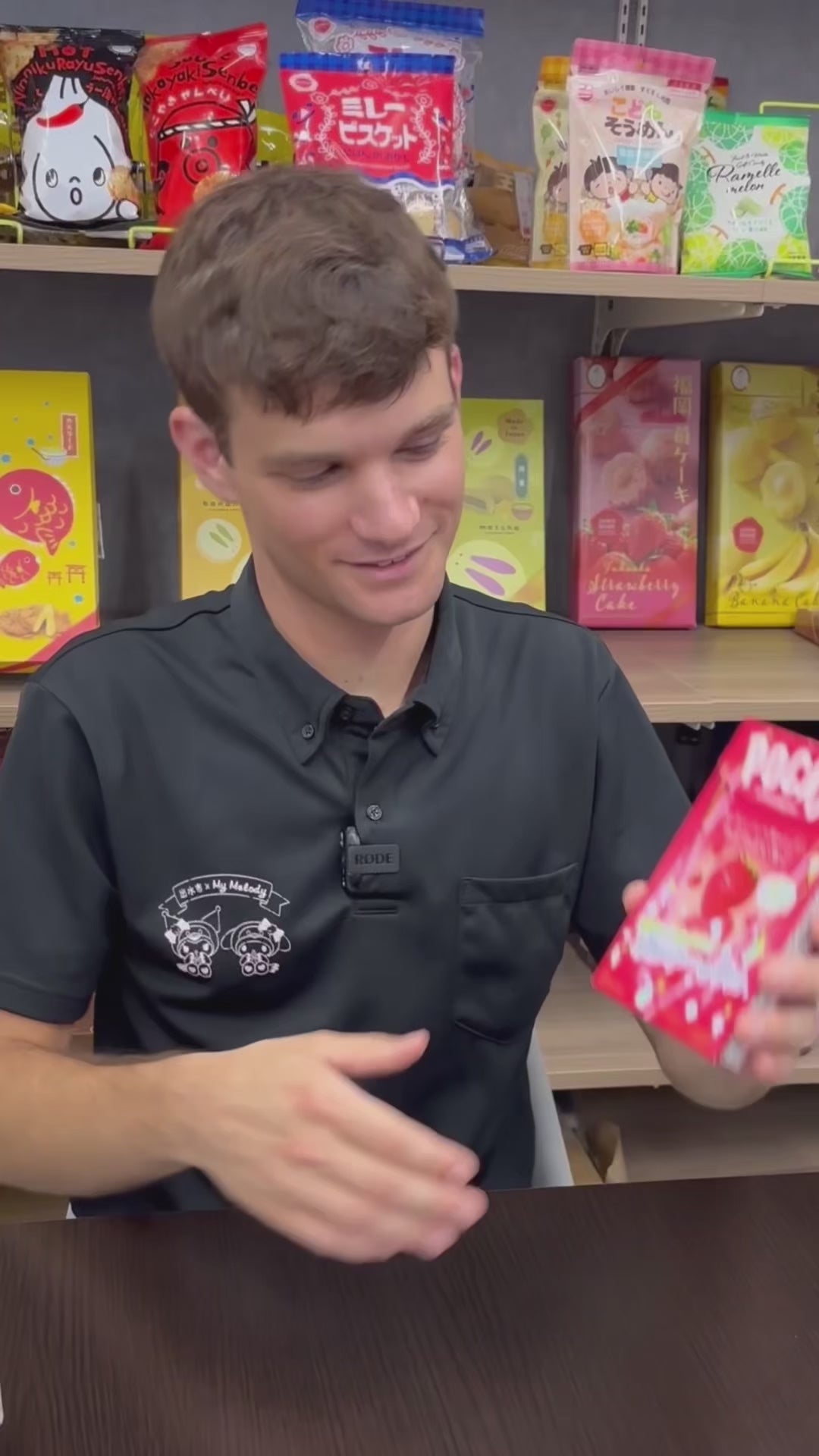 Person holding a box of strawberry-flavored Pocky sticks in a shop with various snack packaging in the background.