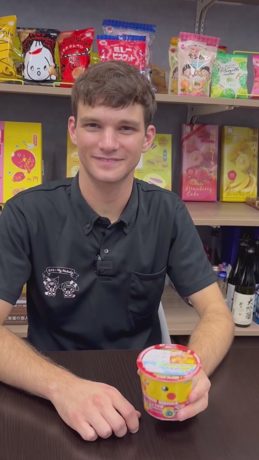 Man holding Ramen Sapporo Ichiban Pokemon Noodle cup with Pikachu design, soy sauce flavored, displayed in a store setting.