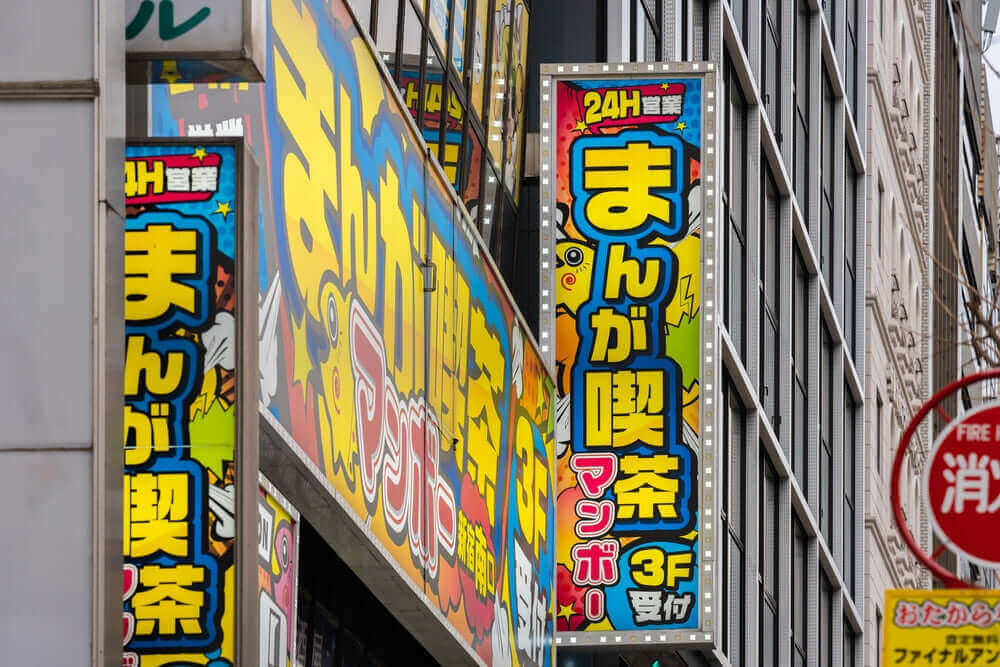 Colorful signs of a 24-hour manga café in Japan's urban area, highlighting vibrant atmosphere and non-stop access for manga lovers.