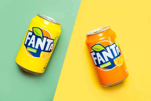 Two Fanta soda cans, one lemon and one orange flavor, on a colorful background. Explore popular Fanta varieties and flavors.